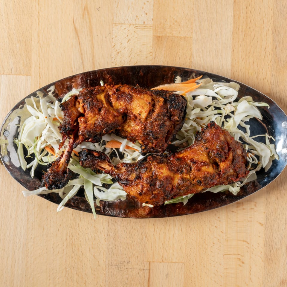 Two pieces of tandoori chicken on a bed of shredded cabbage and carrots, on a metal platter.