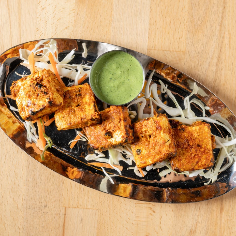Grilled paneer tikka pieces with green chutney, shredded cabbage, and carrots on a silver platter.