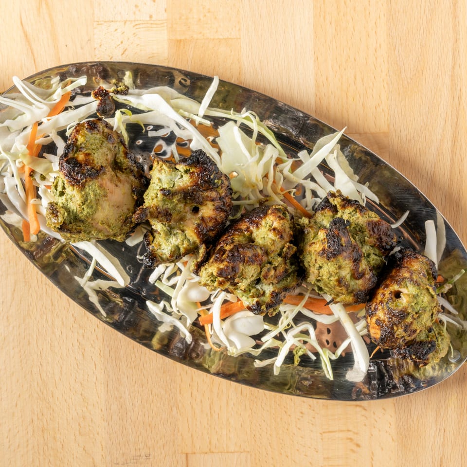 Five pieces of green marinated chicken tikka with charred edges, served on shredded cabbage and carrots.