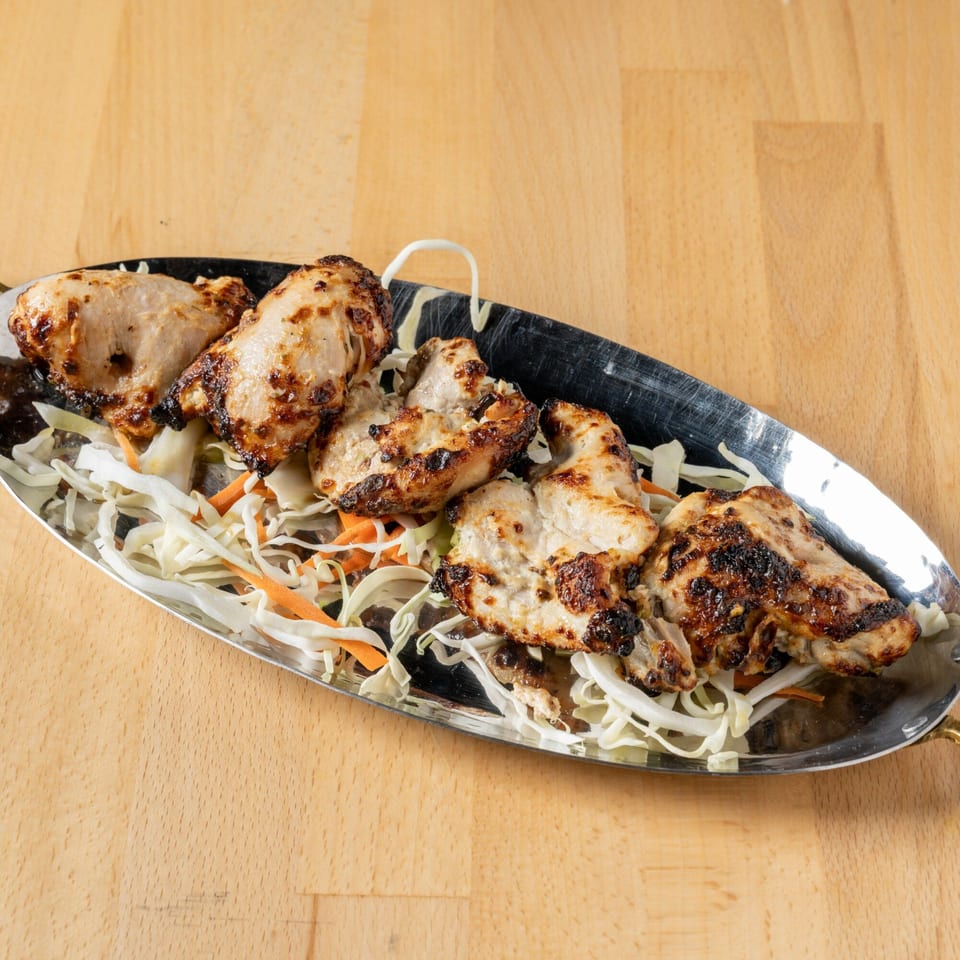 Grilled chicken pieces with charred marks, served on a bed of shredded cabbage and carrots.