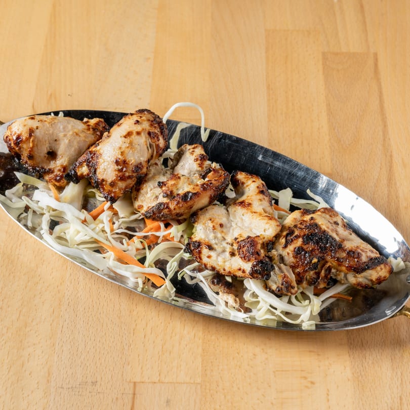 Grilled chicken pieces with charred marks, served on a bed of shredded cabbage and carrots.
